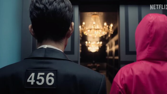 squid game season 3 trailer A still from the Squid Game Season 3 trailer. A man in a black suit with the number 456 on his back, standing next to someone in a pink jumpsuit.