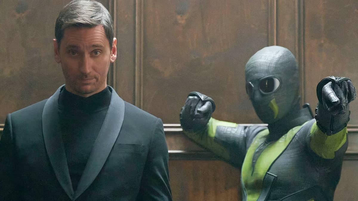 A man in a black jacket standing next to a man in a green and black costume.