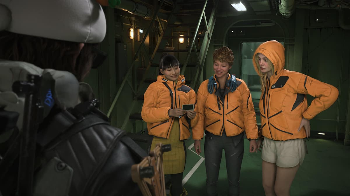 Three women in orange jackets looking at a polaroid picture for our Death Stranding 2 review.