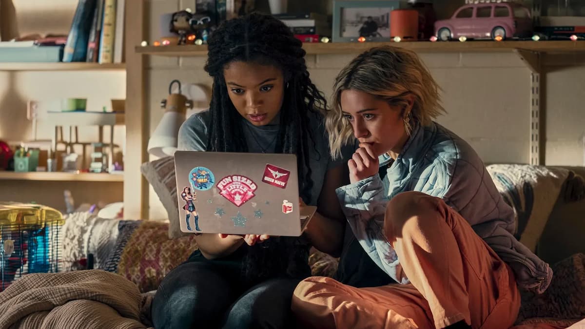 Two girls sitting on a bed looking at a laptop in Gen V.