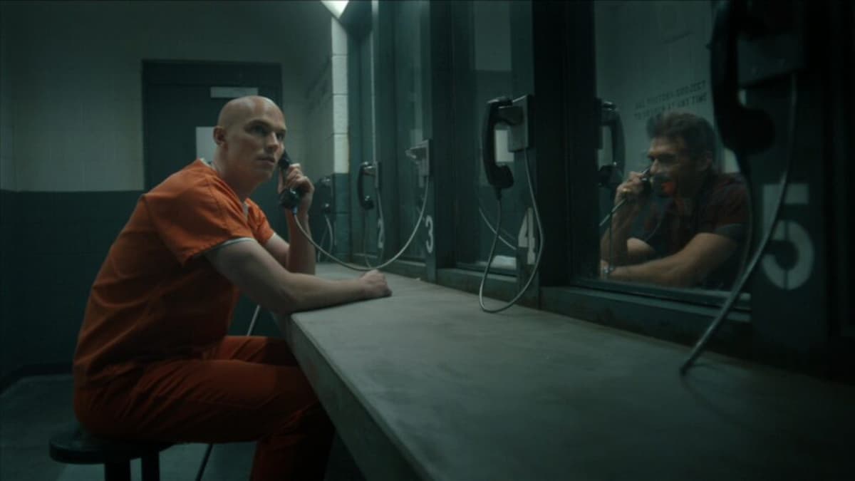 A man in orange prison clothing on the phone in Peacemaker Season 2.
