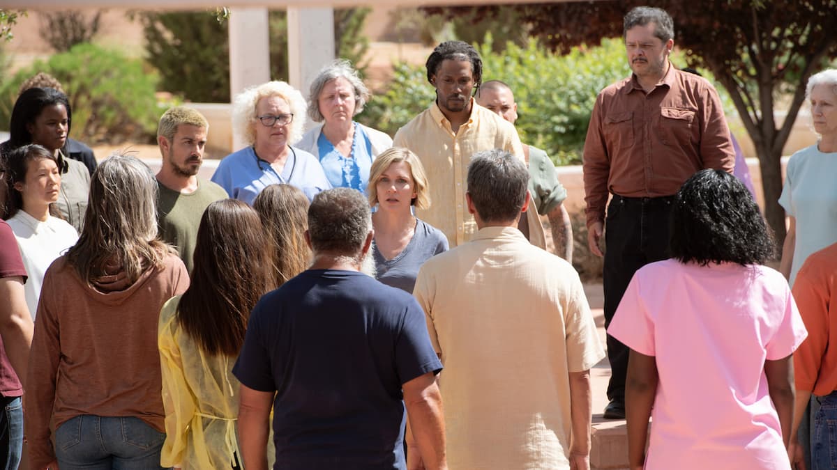 A blonde woman surrounded by a group of people in Pluribus.