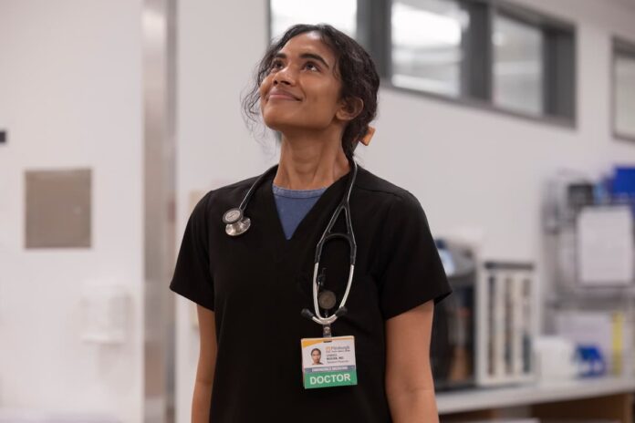 pitt supriya ganesh A doctor in black scrubs looking upwards and smiling. Supriya Ganesh in The Pitt.
